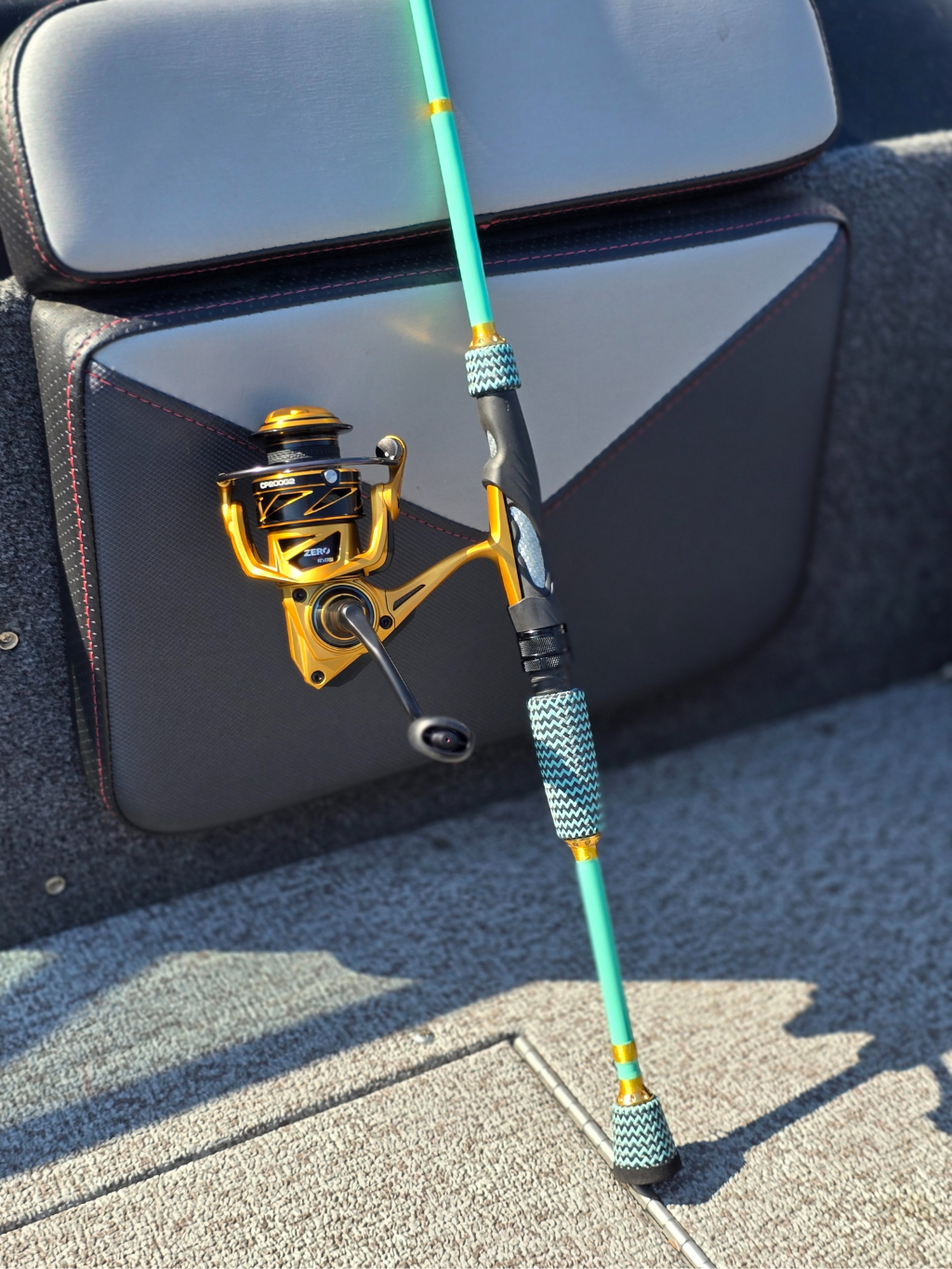 Canne à pêche turquoise et or Les Cannes Boréal avec moulinet doré, poignée texturée et détails haut de gamme, posée dans un bateau.