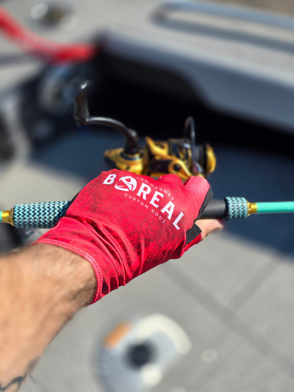 Gant de pêche Boréal rouge avec protection UV porté sur une canne à pêche avec moulinet spinning, utilisé sur un bateau.