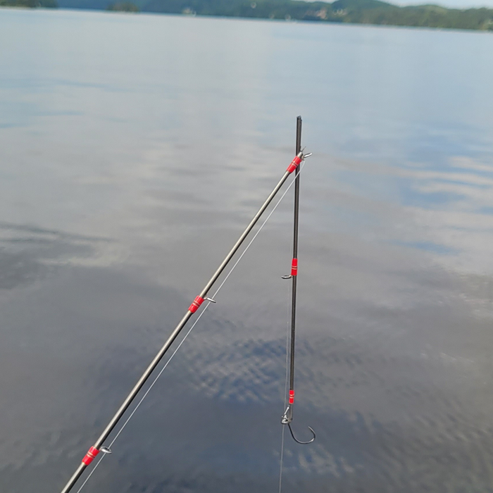 Canne à pêche brisée au niveau du dernier anneau, flottant au-dessus d’un lac calme avec des rives boisées en arrière-plan.